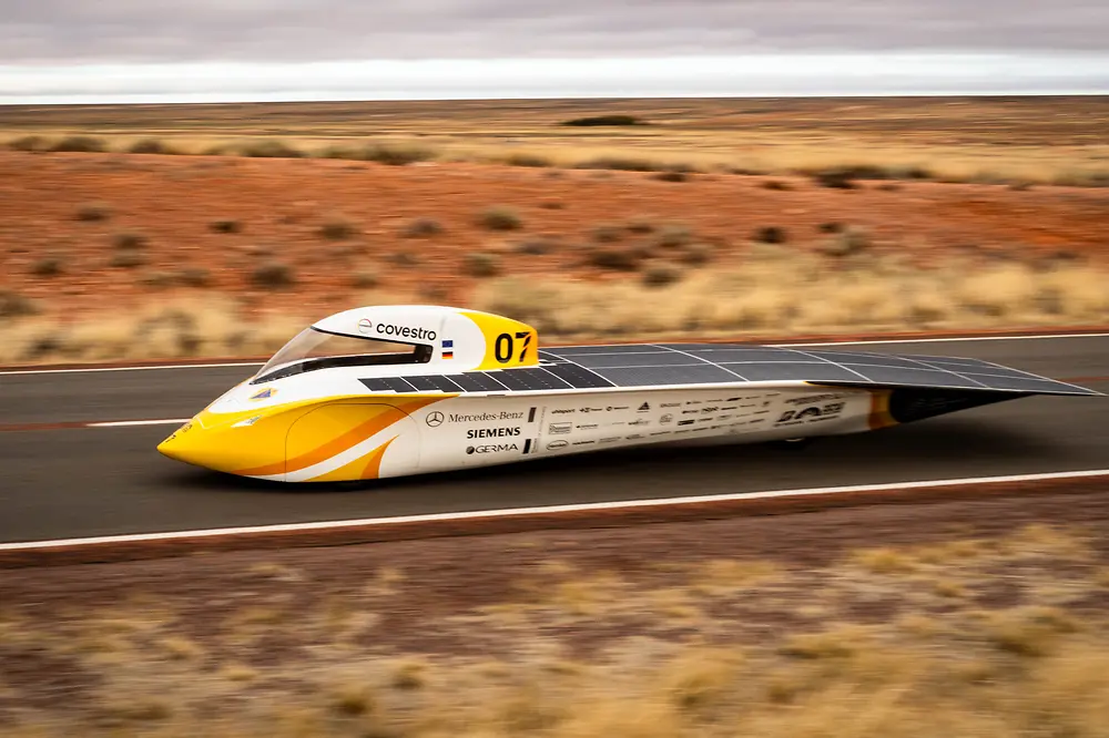 Gelb-weißer Solarwagen „Aethon“ des Aachener Studententeams mit sichtbaren Sponsorenlogos fährt durch das rote australische Outback; an Bord sind Hochleistungsklebstoffe von Henkel zur Sicherstellung von Top-Performance.