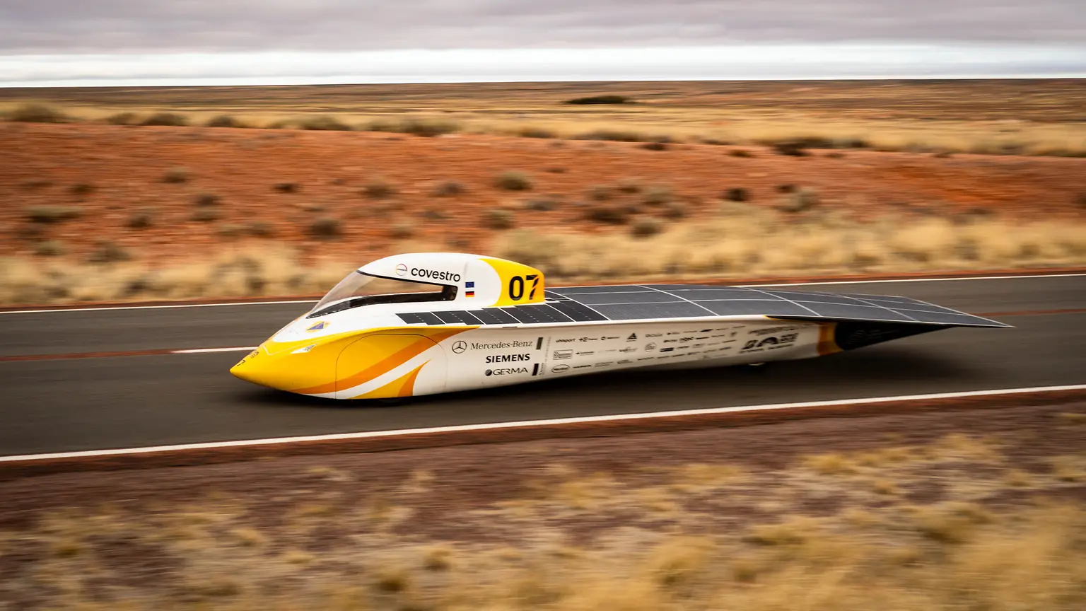 Gelb-weißer Solarwagen „Aethon“ des Aachener Studententeams mit sichtbaren Sponsorenlogos fährt durch das rote australische Outback; an Bord sind Hochleistungsklebstoffe von Henkel zur Sicherstellung von Top-Performance.