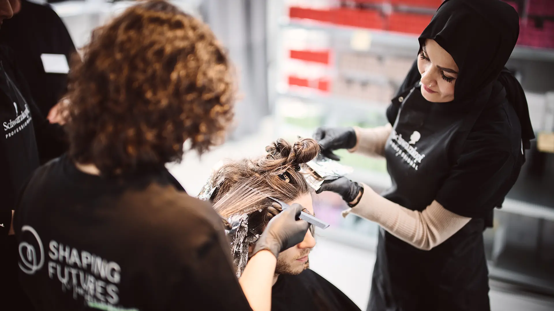 Tamana färbt gemeinsam mit einer weiteren Teilnehmerin die Haare eines Modells.