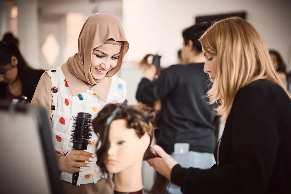 Zwei Frauen frisieren im Rahmen des Programms von Shaping Futures einen Übungskopf