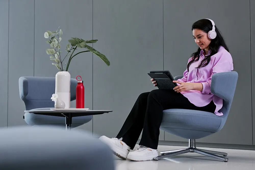 Ein Foto einer Frau, die in einem Loungesessel sitzt, sich auf ihr Tablet konzentriert und Kopfhörer trägt.