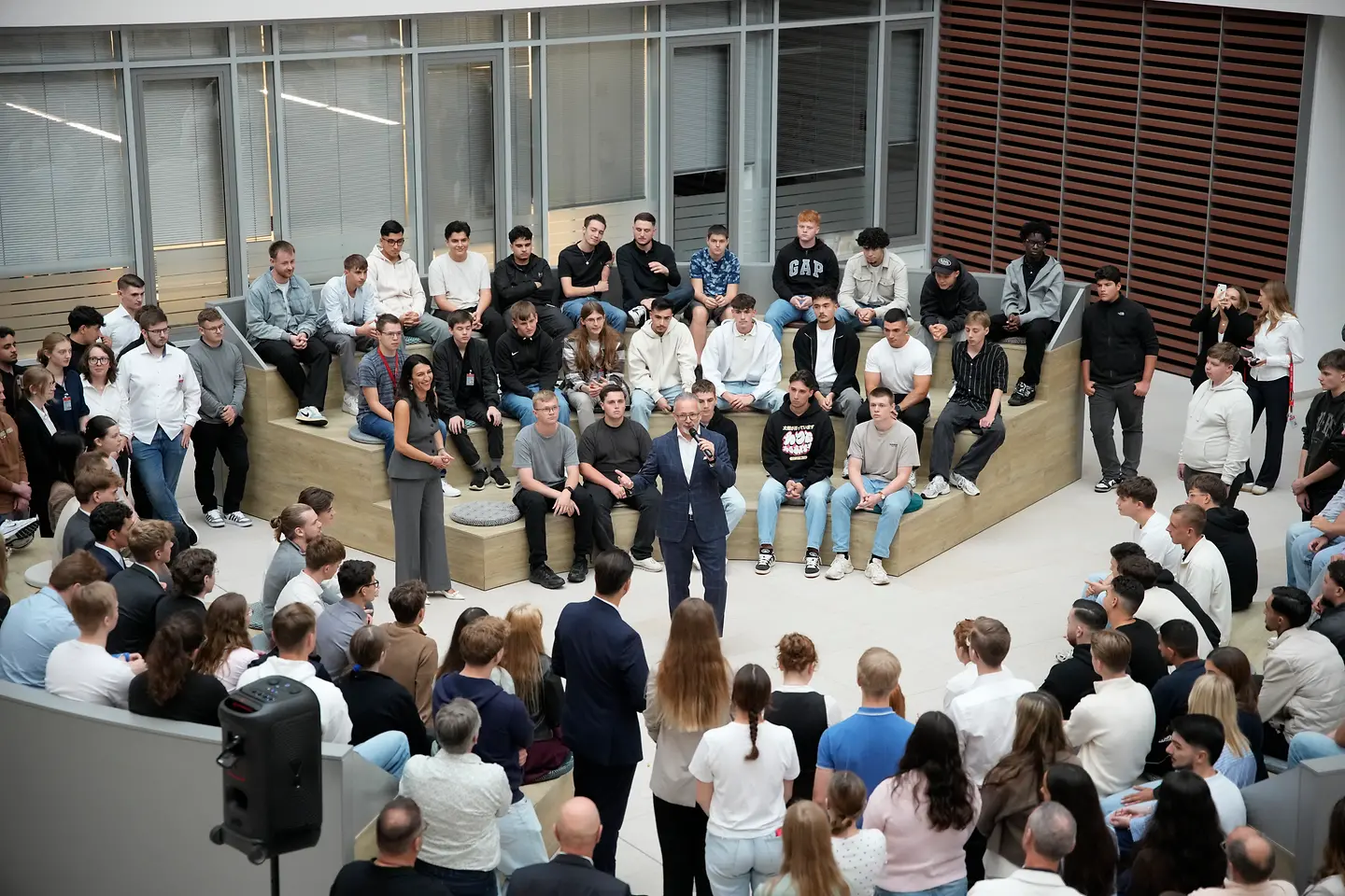 Henkel CEO Carsten Knobel steht im Rondel und spricht zu den neuen Auszubildenden und dual Studierenden beim Ausbildungsstart 2025. Die jungen Talente sitzen auf Stufen im Halbkreis um ihn herum, während weitere Teilnehmende im Raum stehen.