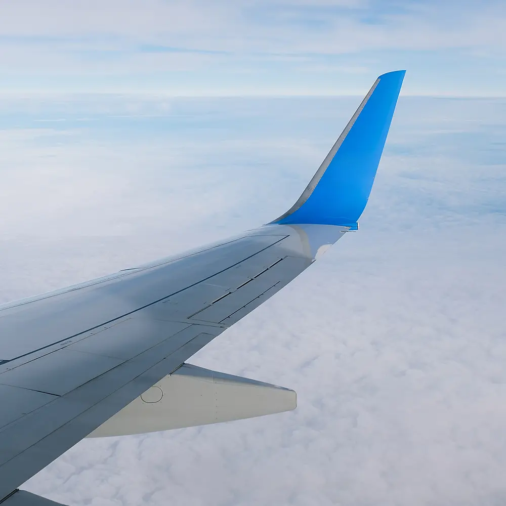 Ein Flugzeugflügel mit einem blauen Winglet über den Wolken.
