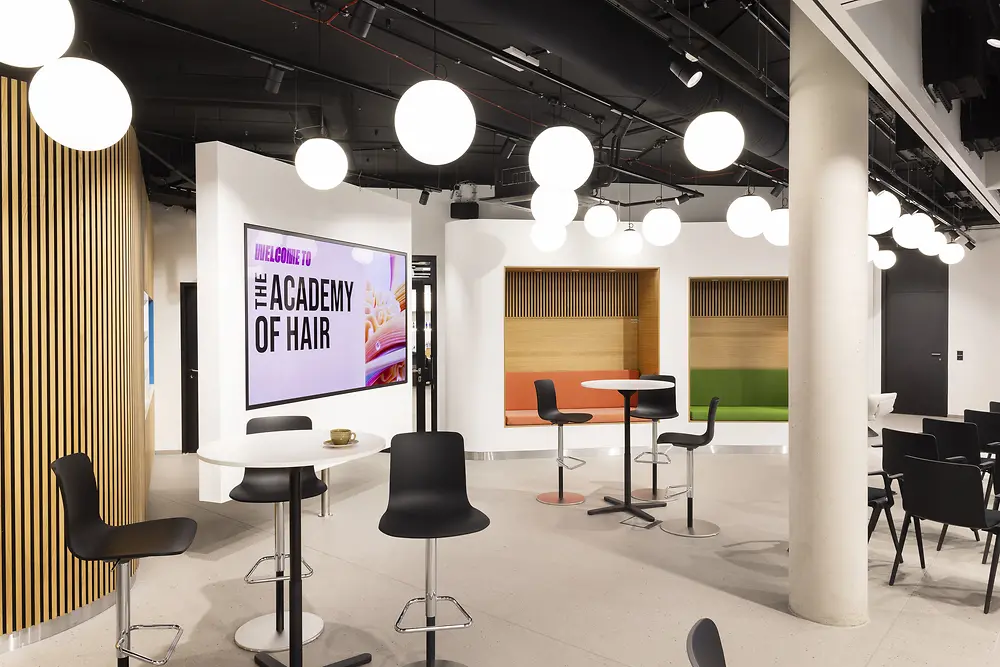 Das Foto zeigt einen Einblick in die Academy of Hair in Hamburg mit mehren runden Tischen und Sitznischen. 