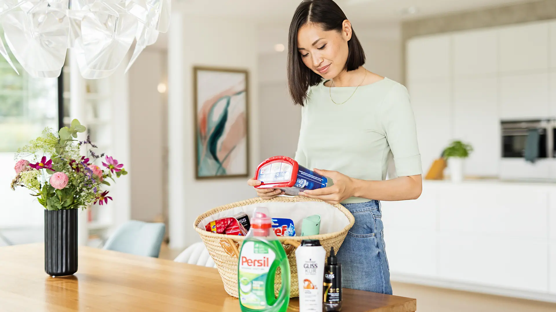 Frau mit Einkaufskorb voller Henkel Produkte wie Persil, Gliss, Bref, Somat, taft, etc.