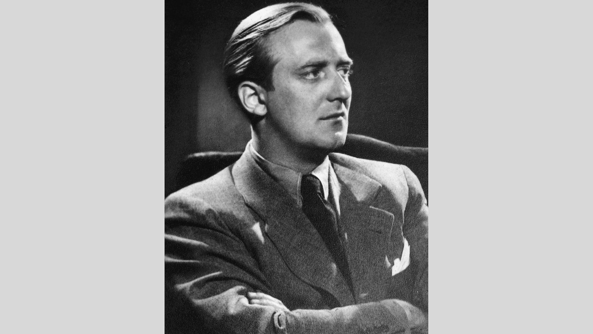 Schwarz-weiß Portrait von Werner Lüps. Er sitzt der Kamera abgewandt mit verschränkten Armen in einem Sessel und schaut rechts an der Kamera vorbei.