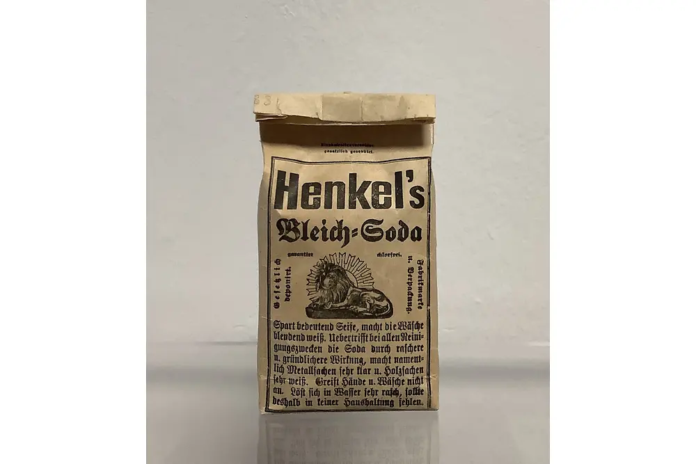 Braune Papierverpackung des Produkts „Henkel’s Bleich-Soda“ mit schwarzer Schrift und einer Illustration eines Löwen. Das Produkt steht auf einer glatten Oberfläche.