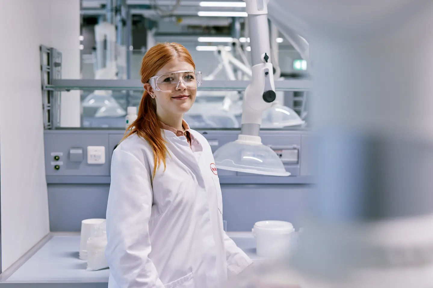 Ein Absolvent startet seine Karriere bei Henkel, trägt einen weißen Laborkittel und steht in einer modernen Laborumgebung mit technischem Equipment im Hintergrund.