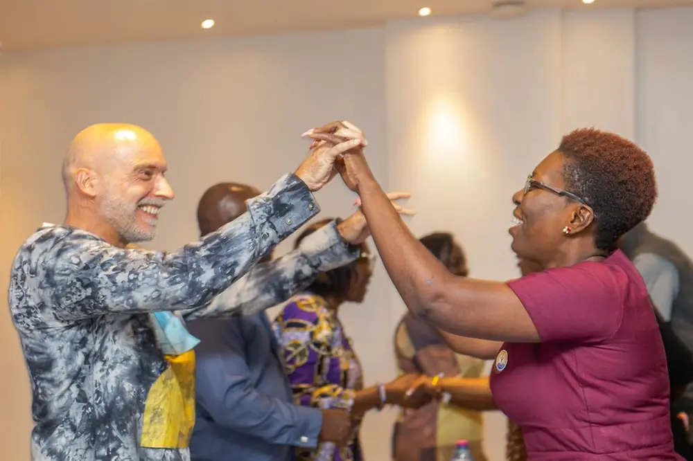 Zwei Personen stehen einander gegenüber, mit ineinander verschränkten Händen in einer nach oben gerichteten Geste.