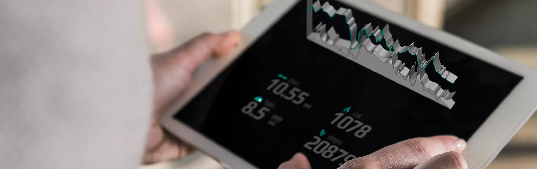 A person holding a tablet displaying digital charts and numeric data, viewed from over the shoulder in a bright indoor setting.