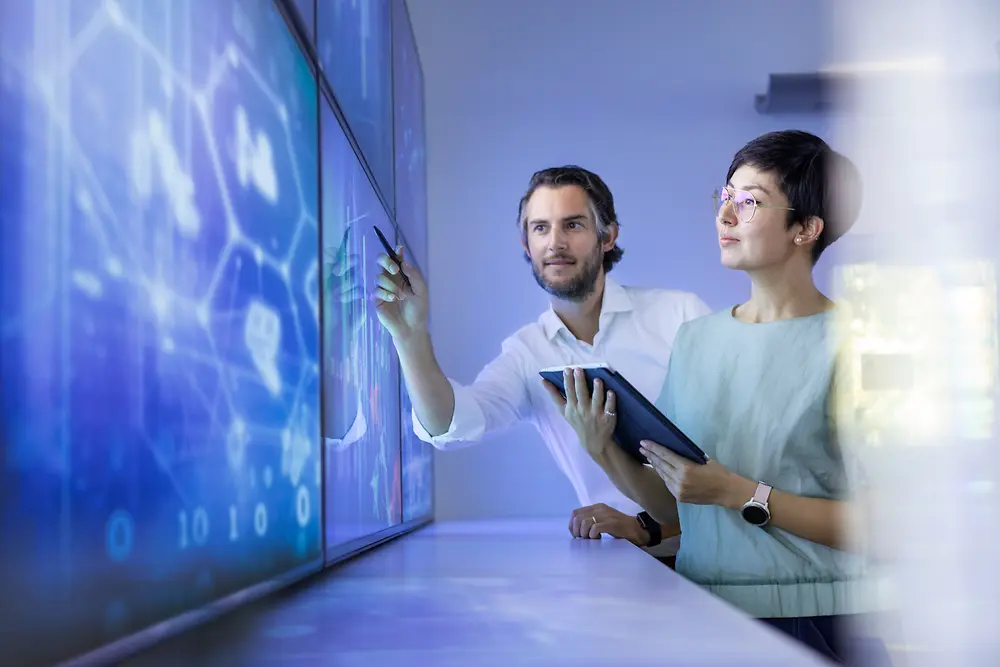 
Two colleagues analyzing digital data on a large screen in a modern tech workspace