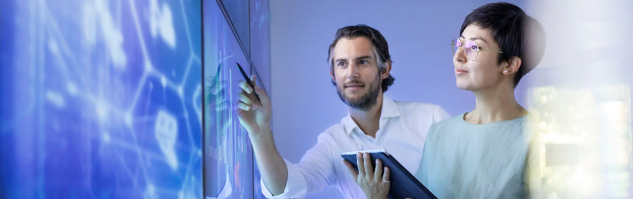 
Two colleagues analyzing digital data on a large screen in a modern tech workspace