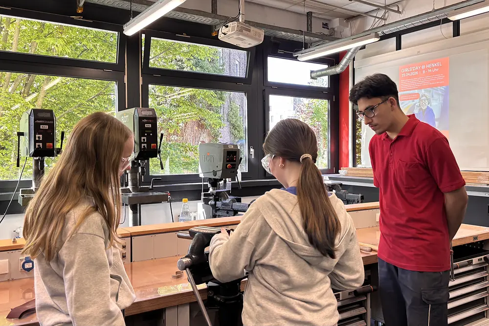 Zwei Mädchen arbeiten in einer Werkstatt an einer stationären Maschine.