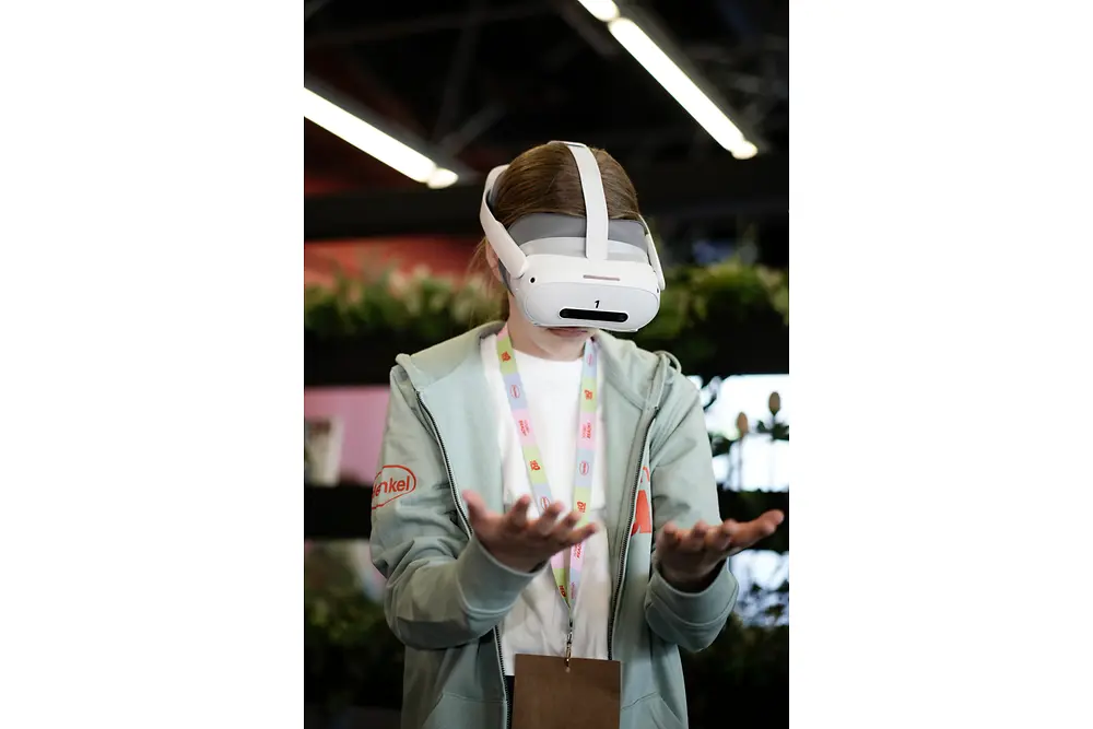 Ein Mädchen steht mit einer VR-Brille im Raum und blickt auf ihre Hände. 