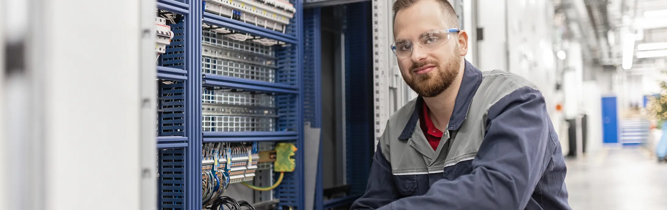 Junge Mitarbeitende mit Schutzbrille und blauer Arbeitskleidung an einem Produktionsstandort