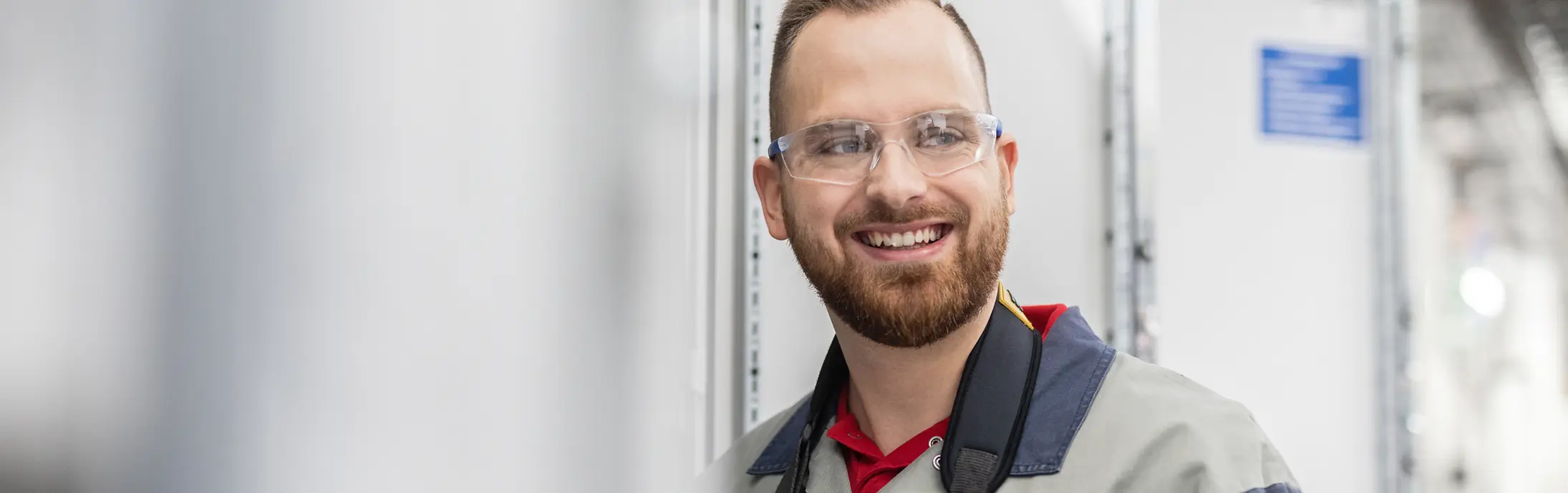 Junge Mitarbeitende mit Schutzbrille und blauer Arbeitskleidung an einem Produktionsstandort