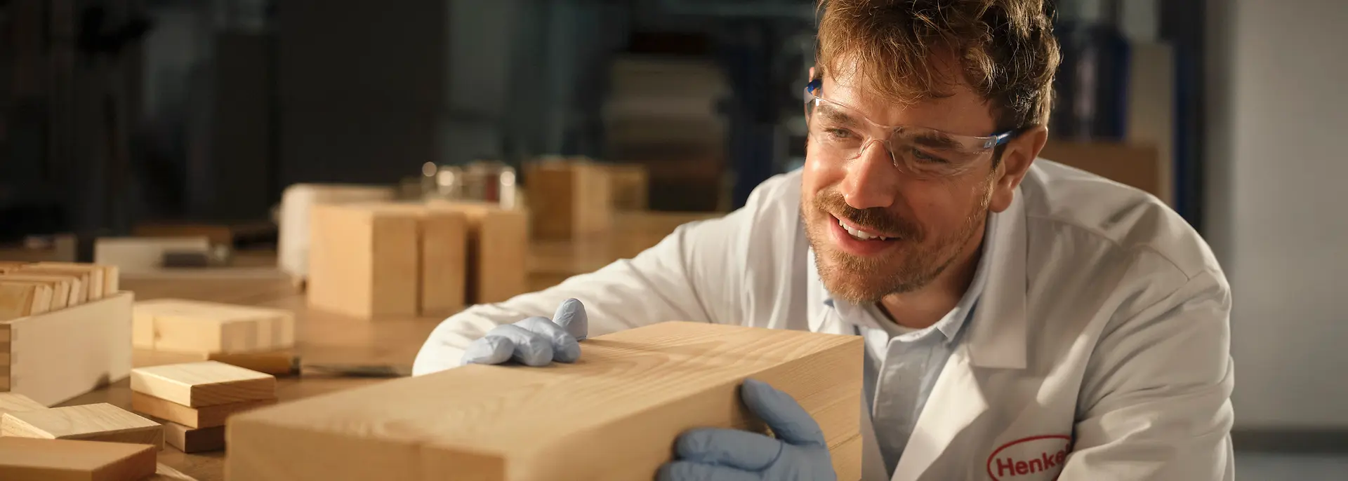 Person in einem Henkel-Labor untersucht einen rechteckigen Holzblock auf einem Arbeitstisch.