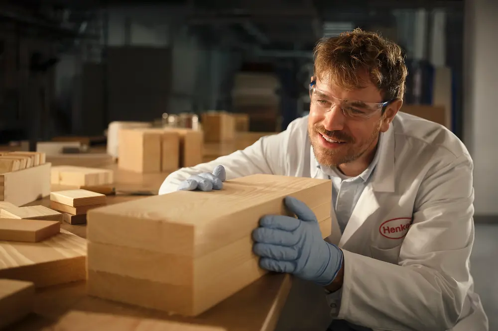 Person in einem Henkel-Labor untersucht einen rechteckigen Holzblock auf einem Arbeitstisch.