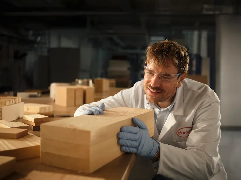 Person in einem Henkel-Labor untersucht einen rechteckigen Holzblock auf einem Arbeitstisch.