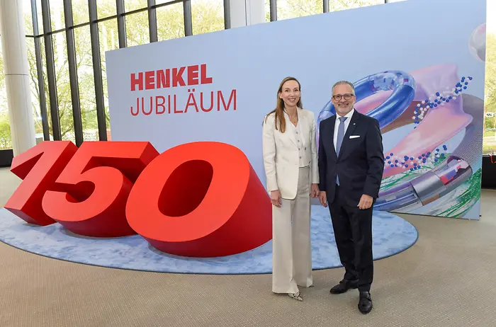 Zwei Personen stehen vor einer großen roten „150“ und einer Jubiläumswand.