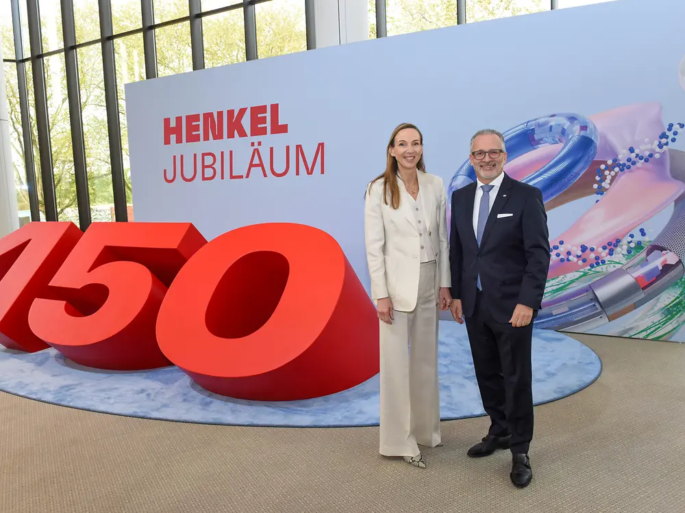 Zwei Personen stehen vor einer großen roten „150“ und einer Jubiläumswand.