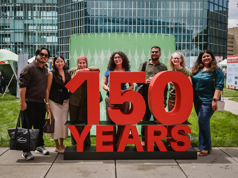 Eine Gruppe von Mitarbeitenden steht vor einer großen roten „150 Years“-Jubiläumsinstallation auf dem Festivalgelände.