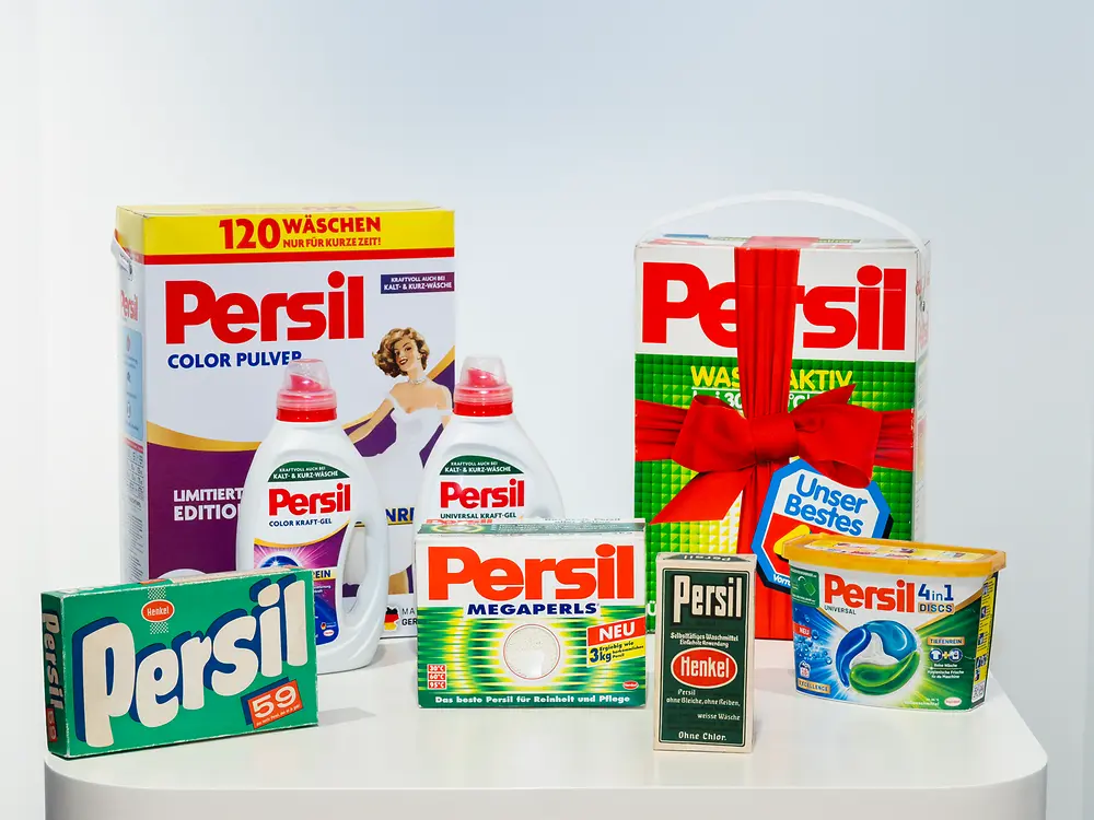 Historische und aktuelle Persil-Produkte nebeneinander präsentiert, darunter Waschmittelpackungen, Flüssigwaschmittel und Produktbehälter in unterschiedlichen Verpackungsdesigns.