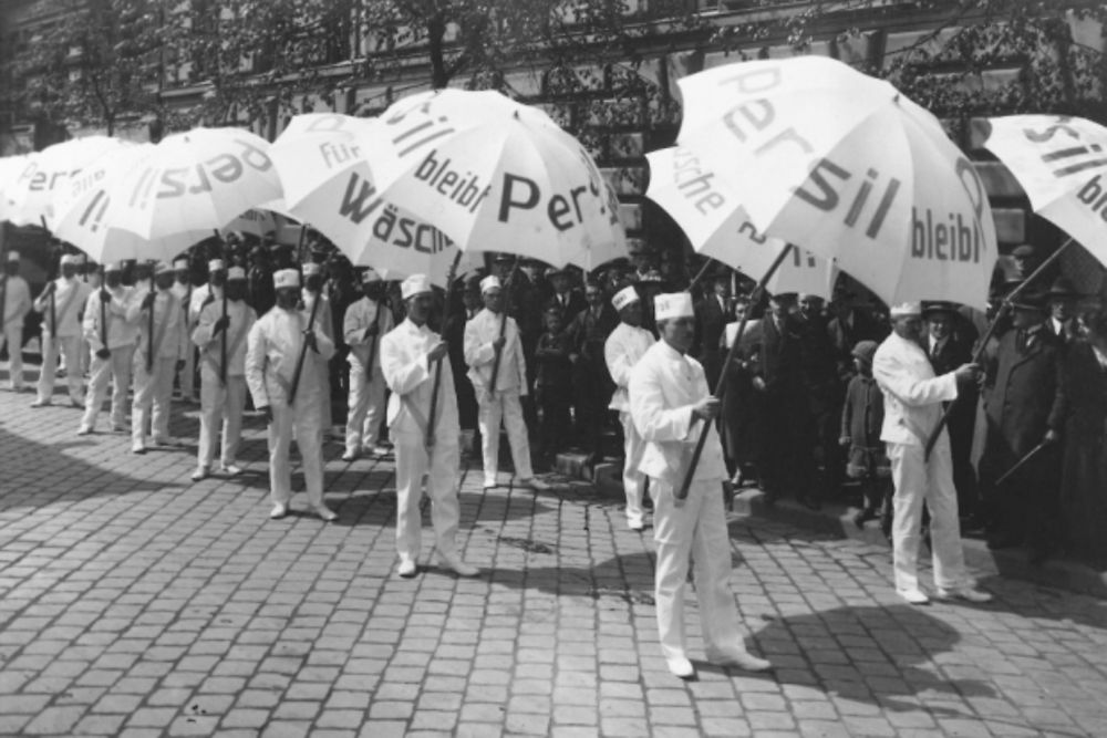 Weiß gekleidete Männer mit Persil-Sonnenschirmen